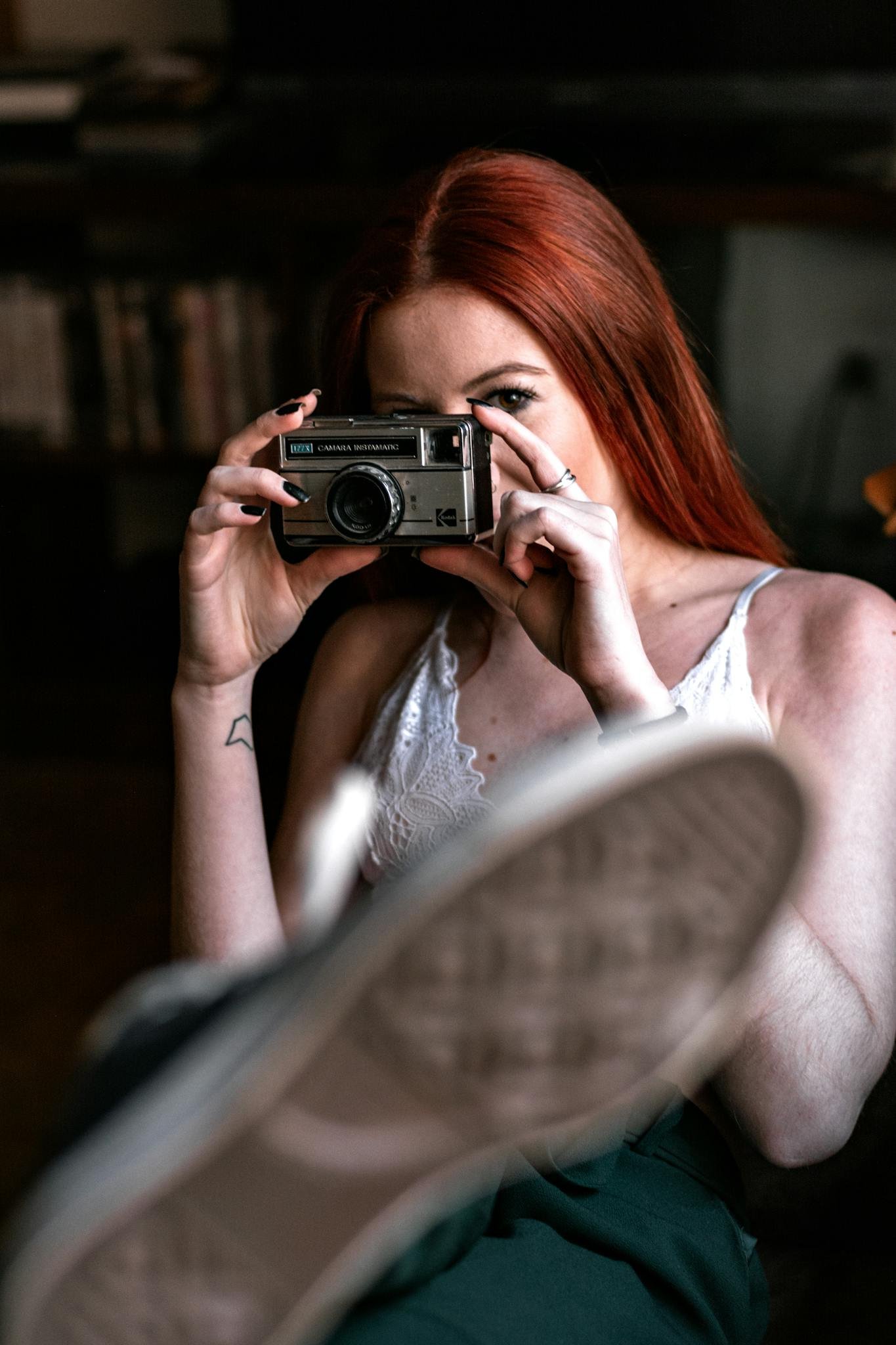 A redheaded woman captures a moment with a vintage camera, emphasizing retro vibes.