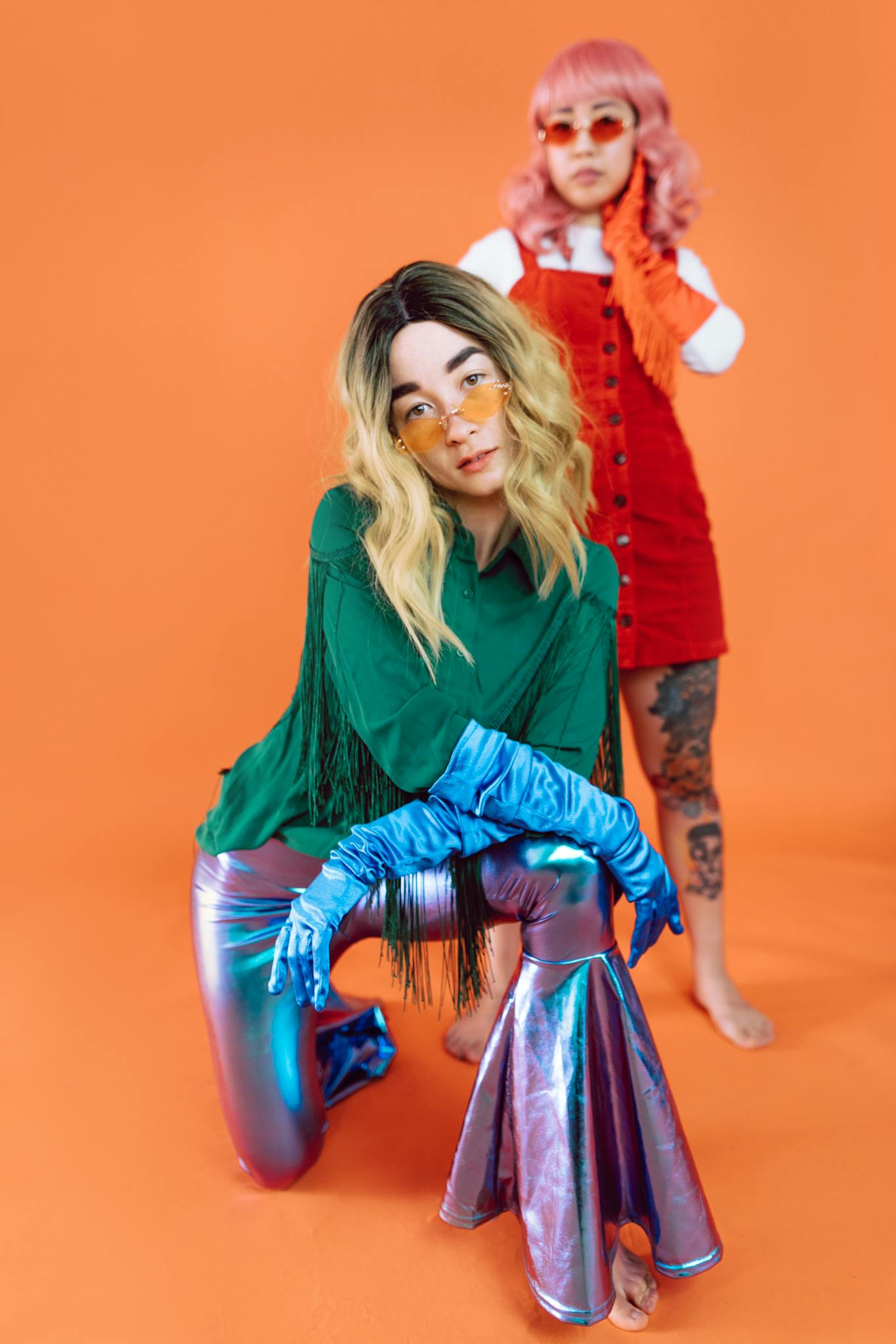 Two models showcasing vibrant retro fashion against an orange backdrop.